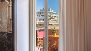 Habitación de hotel con un amplio ventanal corredero que da a un balcón con mobiliario exterior y una planta.