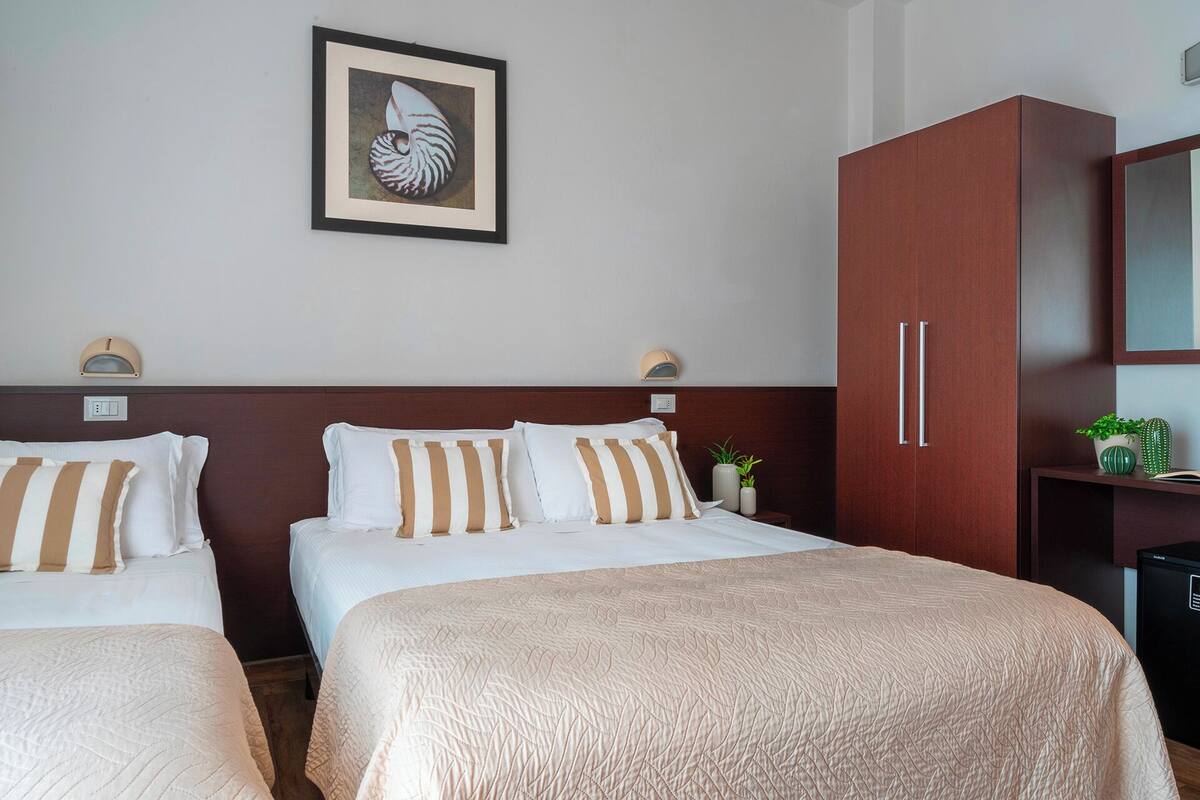 Habitación de hotel con dos camas, un cuadro enmarcado en la pared y un armario con espejo.
