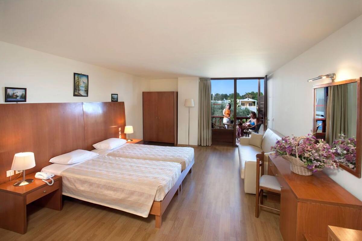 Habitación de hotel con dos camas, un escritorio, una silla, una mesita y un balcón con vistas.