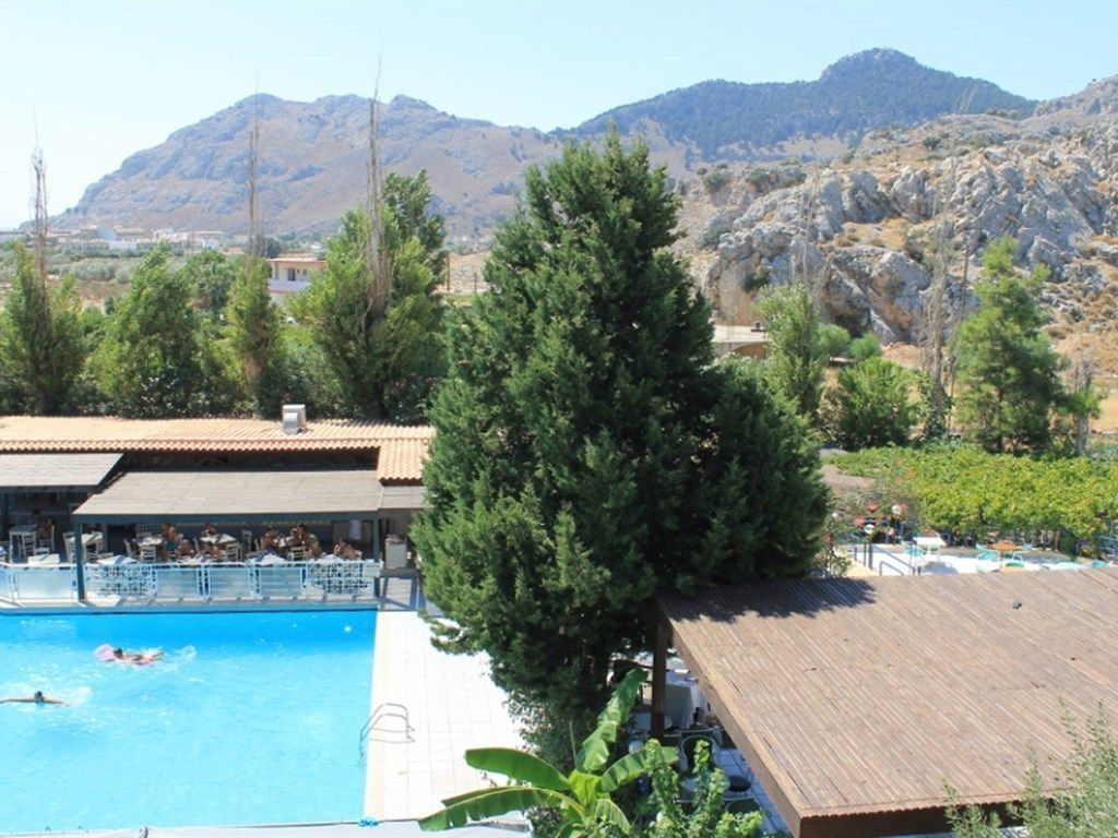 A pool area with a view of mountains, surrounded by trees and a building with a tiled roof.
