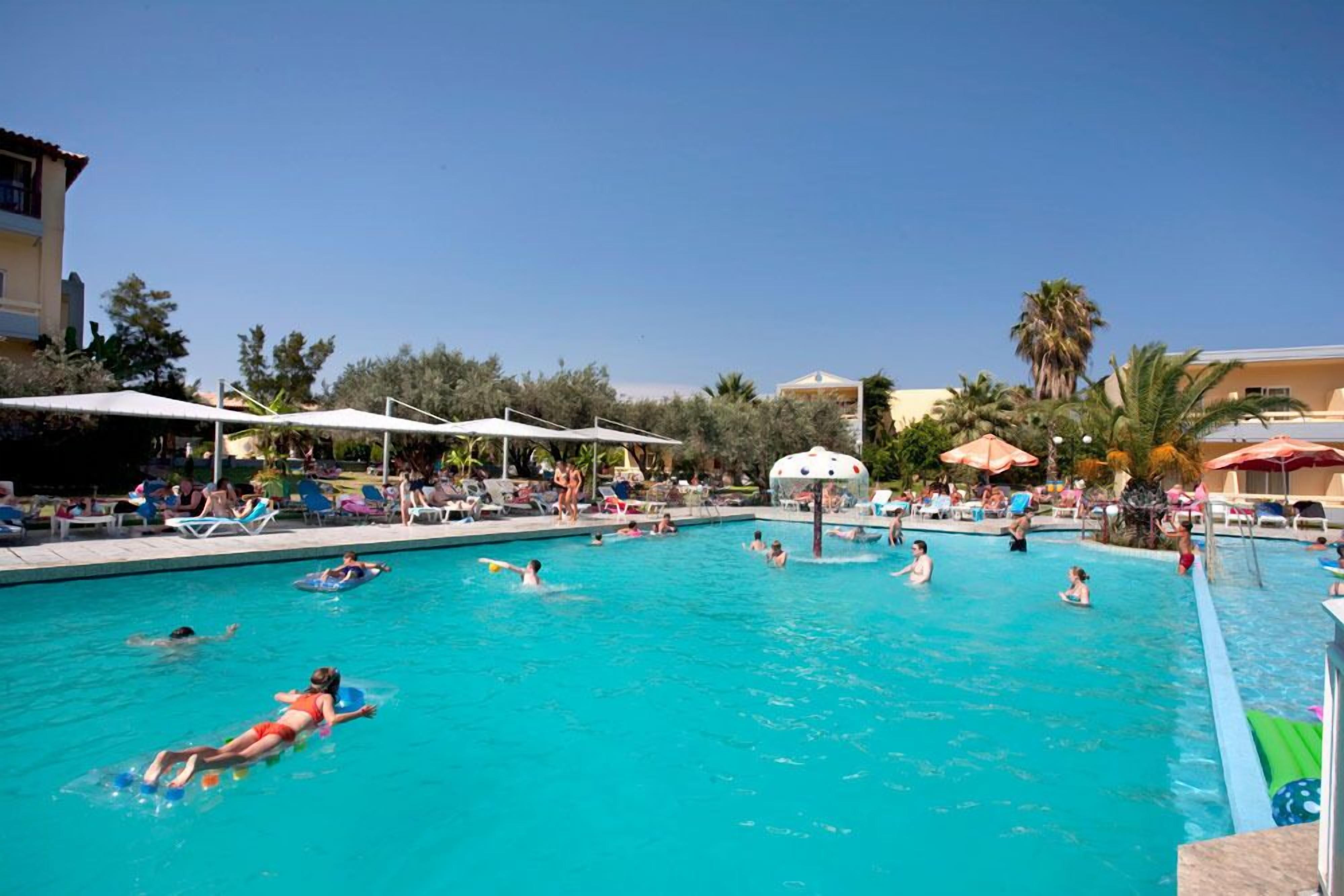 Un espace piscine comprenant plusieurs bassins, des chaises longues, des parasols et des palmiers.