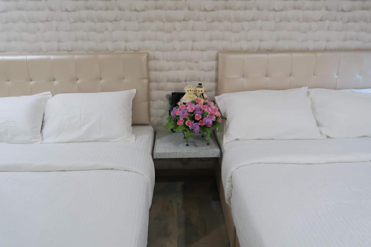 Ein Hotelzimmer mit zwei Betten, jeweils mit weißer Bettwäsche und einem gepolsterten Kopfteil. Zwischen den Betten steht ein kleiner Tisch mit einem Blumenstrauß und einem dekorativen Gegenstand.