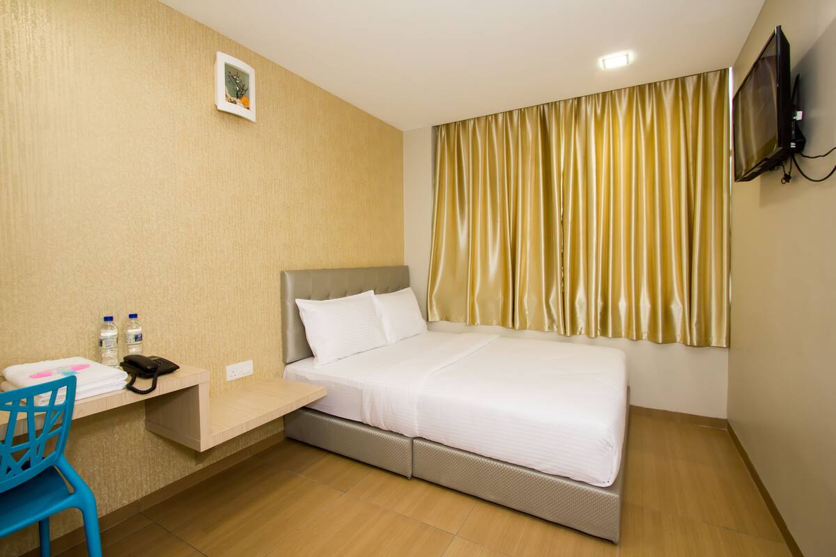 Ein Hotelzimmer mit einem Bett, einem Schreibtisch mit Stuhl, einem Fernseher und einem Fenster mit Vorhängen.