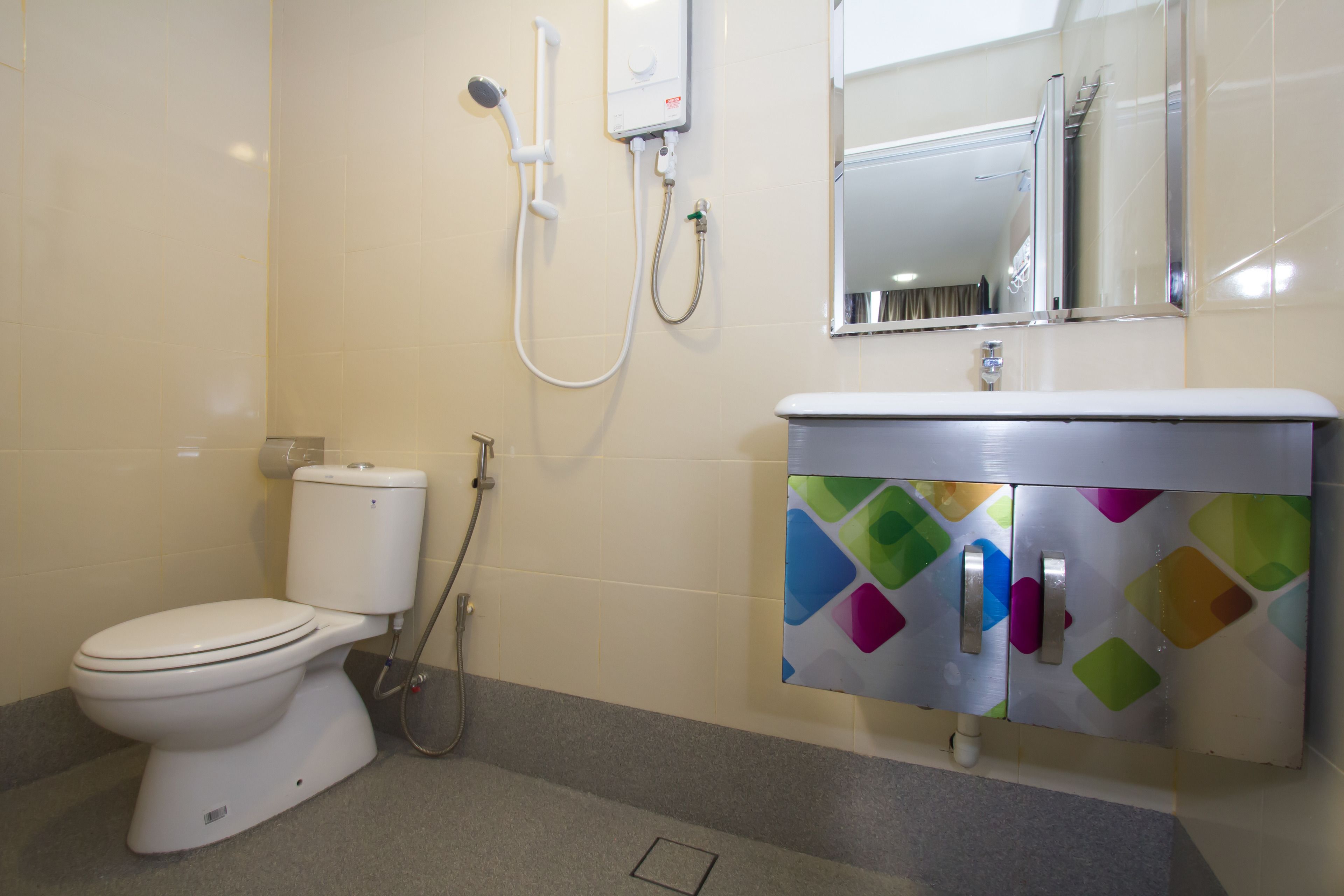 A bathroom with a toilet, a shower, and a sink with a colorful cabinet.