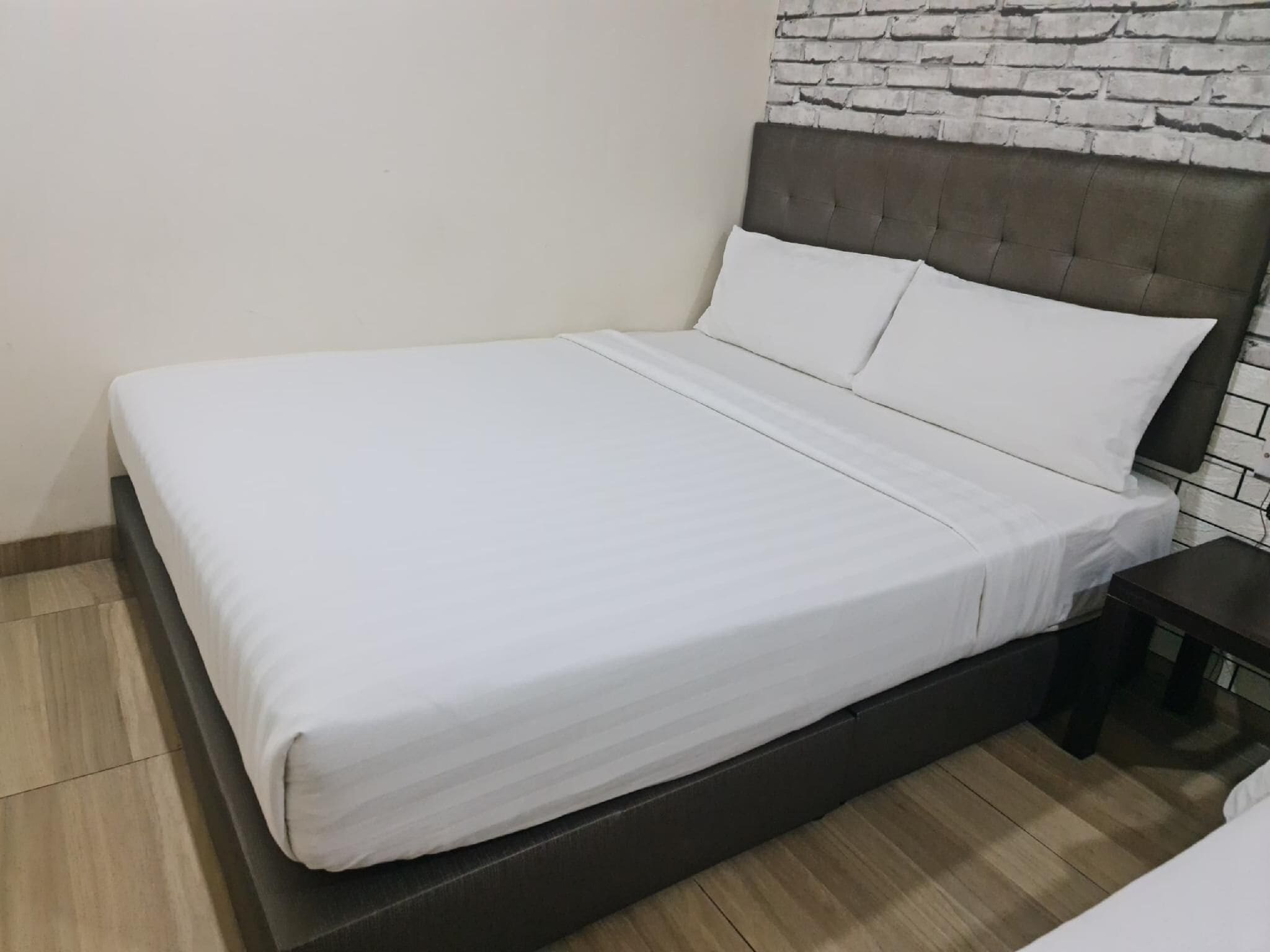 A bed with a white mattress and headboard, a wooden floor, and a brick-patterned wall.