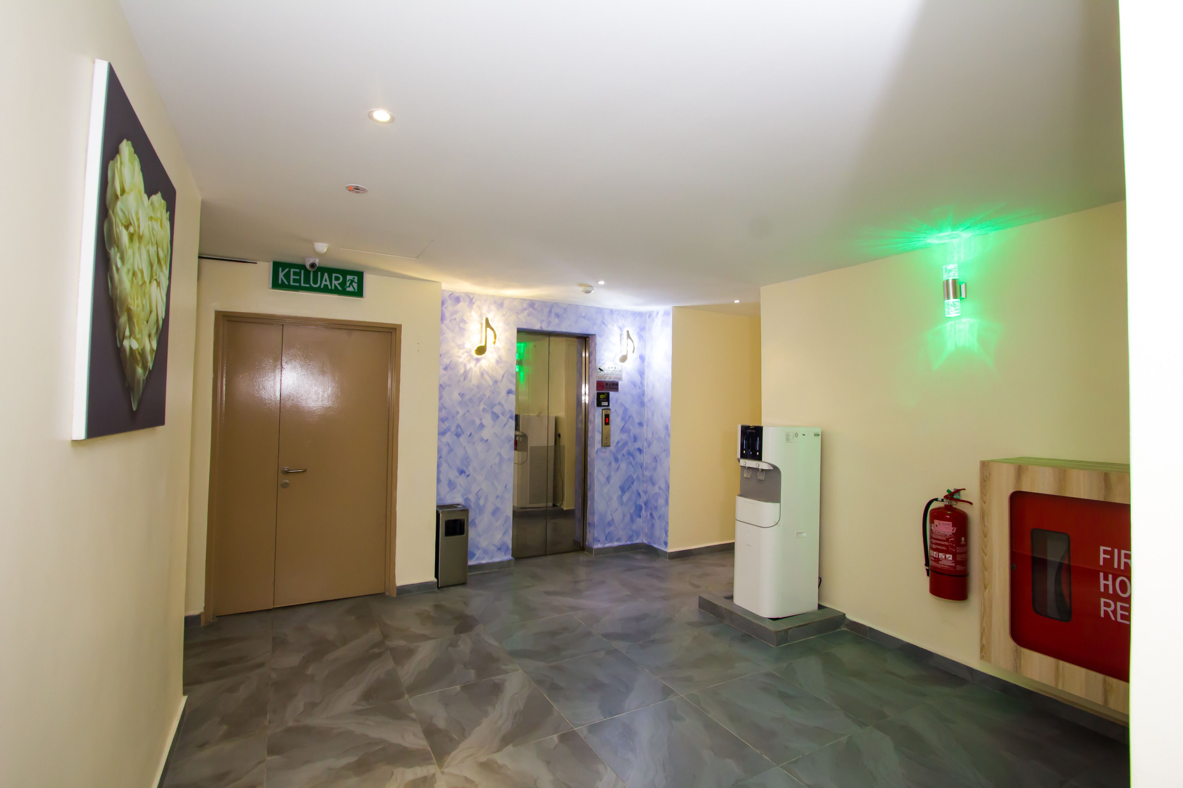 A hotel lobby with a reception desk, a fire extinguisher, and a sign indicating the location of the kitchen.