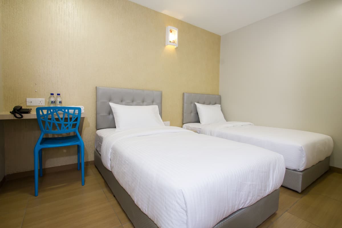 Ein Hotelzimmer mit zwei Betten, einem Schreibtisch mit Stuhl und einer Wandleuchte.