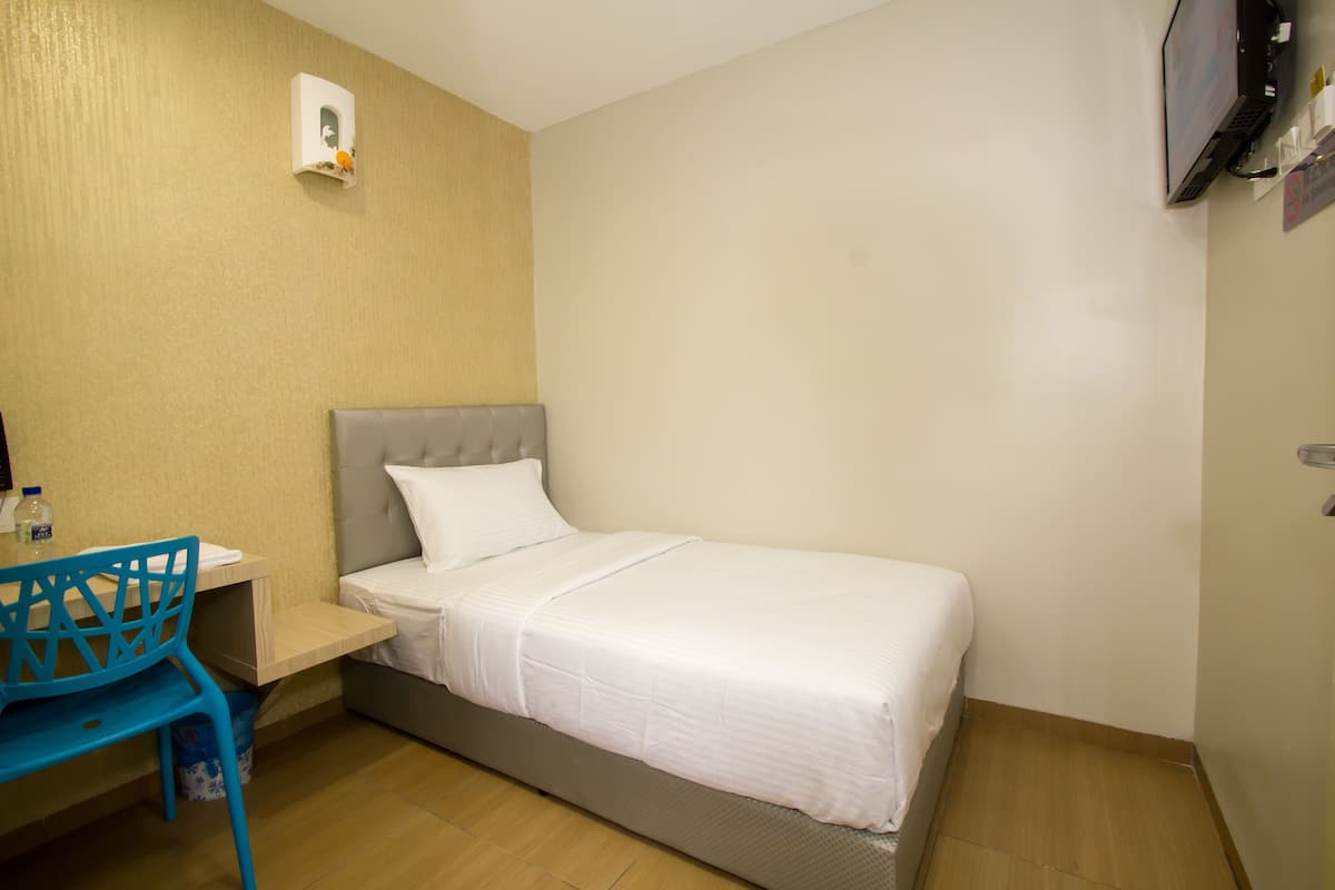Ein Einzelbett mit grauem Kopfteil und weißer Bettwäsche in einem Zimmer mit Holzboden und einem blauen Stuhl.