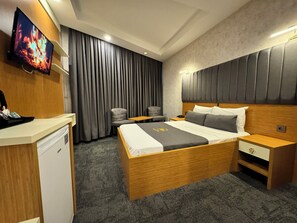 A hotel room with a wooden bed, a desk, a chair, a TV, and a large window with curtains.