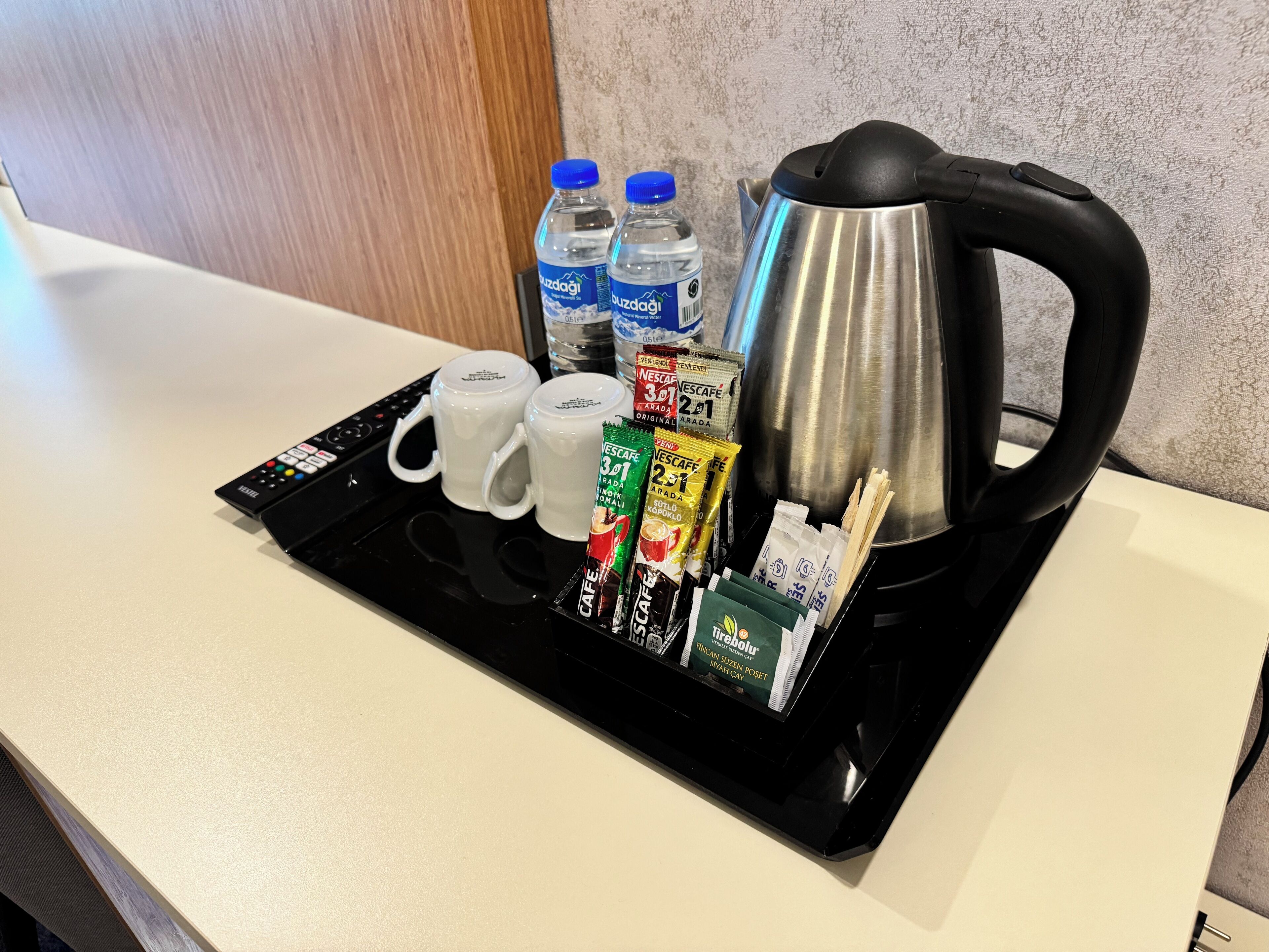 A kitchen counter with a black tray holding a Nescafé coffee maker, two white mugs, two bottles of water, and various coffee pods.