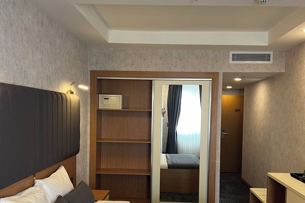A hotel room with a large bed, a wooden nightstand, a desk, a wardrobe, and a mirror.