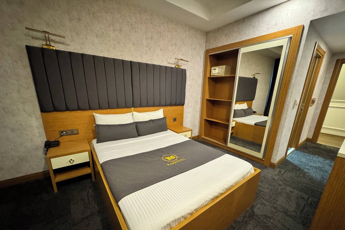 A hotel room with a large bed, a wooden headboard, a wardrobe, and a bedside table.