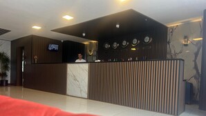 Zona de recepción con diseño moderno, que incluye un mostrador de recepción, una pantalla digital y una pared con relojes.