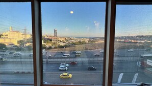 Vista desde una ventana sobre una calle concurrida, coches y un horizonte urbano distante.