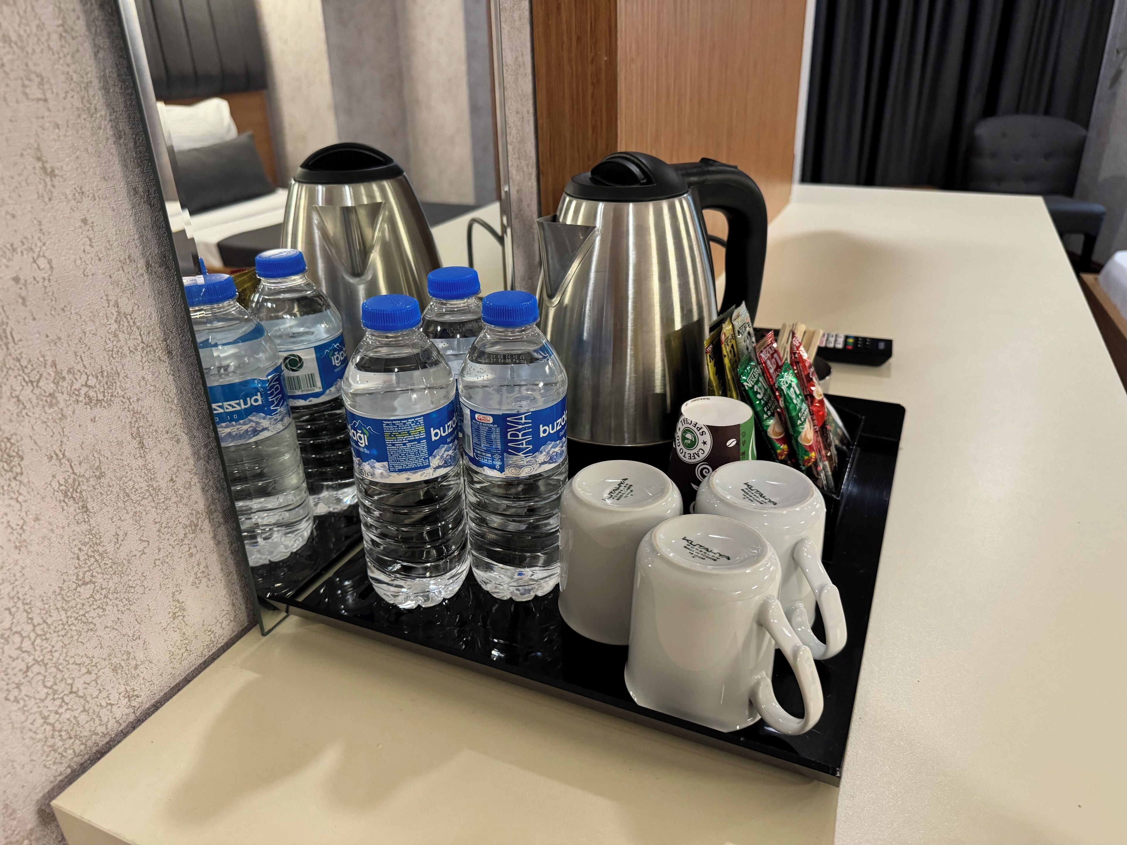 A tray with water bottles, a kettle, and coffee mugs on a hotel counter.