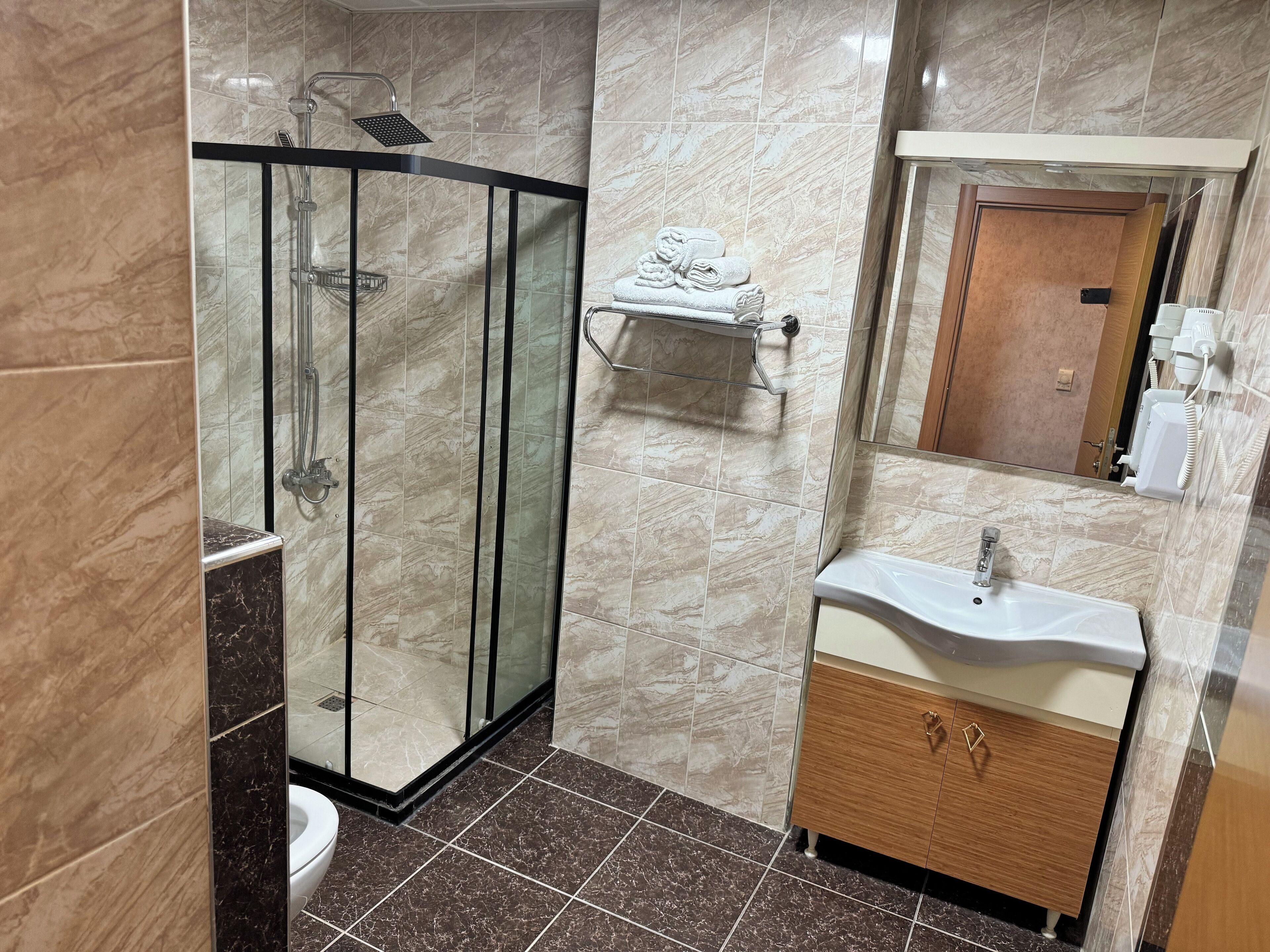 A modern bathroom with a glass-enclosed shower, a toilet, a sink with a vanity, and a towel rack.