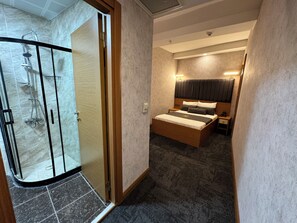 A hotel room with a shower, a bed with a headboard, a nightstand, and a carpeted floor.