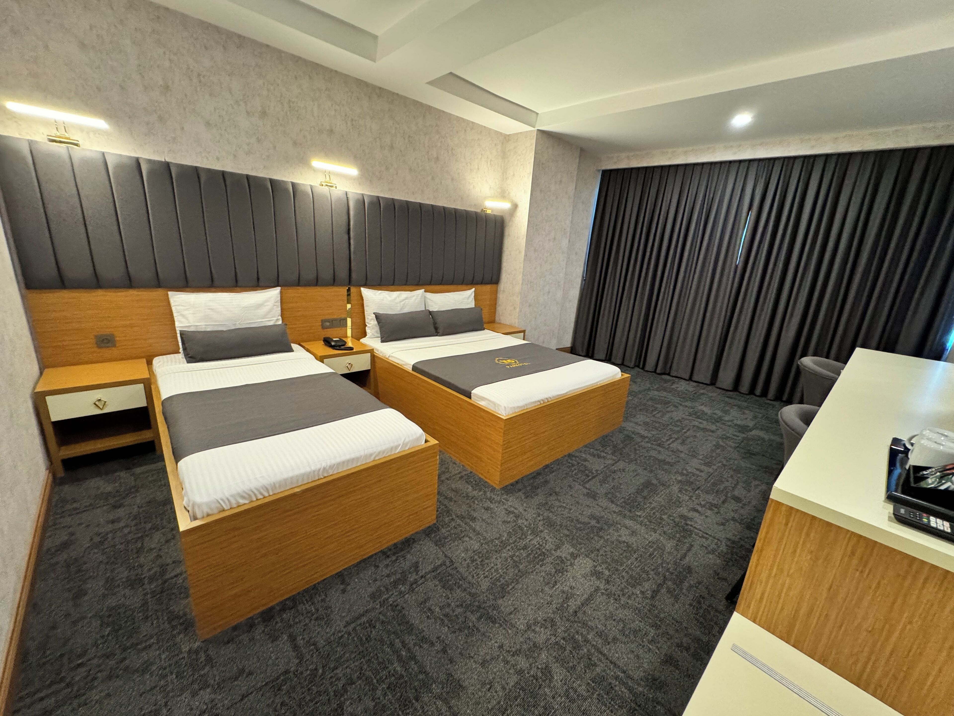 Een hotelkamer met twee houten bedden, een bureau, een stoel en een groot raam met gordijnen.