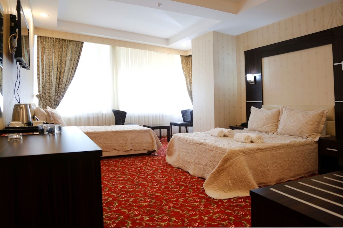 A hotel room with two beds, a desk, a chair, a TV, and a red carpet.