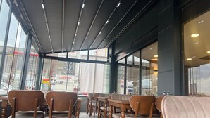 Un restaurante con mesas y sillas de madera, ventanas amplias y un diseño moderno en el techo.
