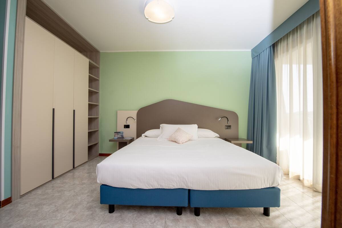 A bedroom with a large bed, a wardrobe, a nightstand, and a lamp.