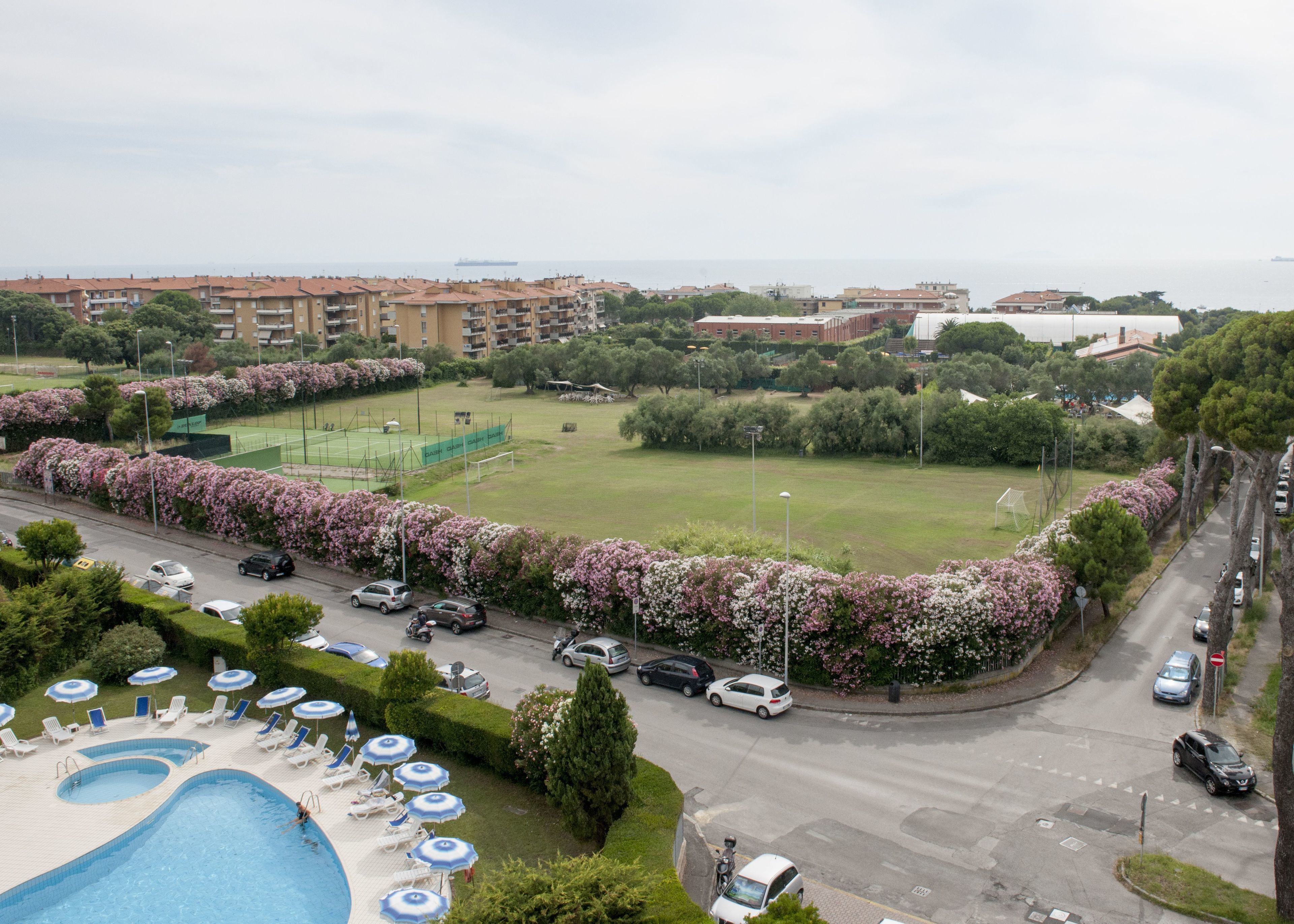 Um hotel com piscina, quadra de tênis e vista para o mar.