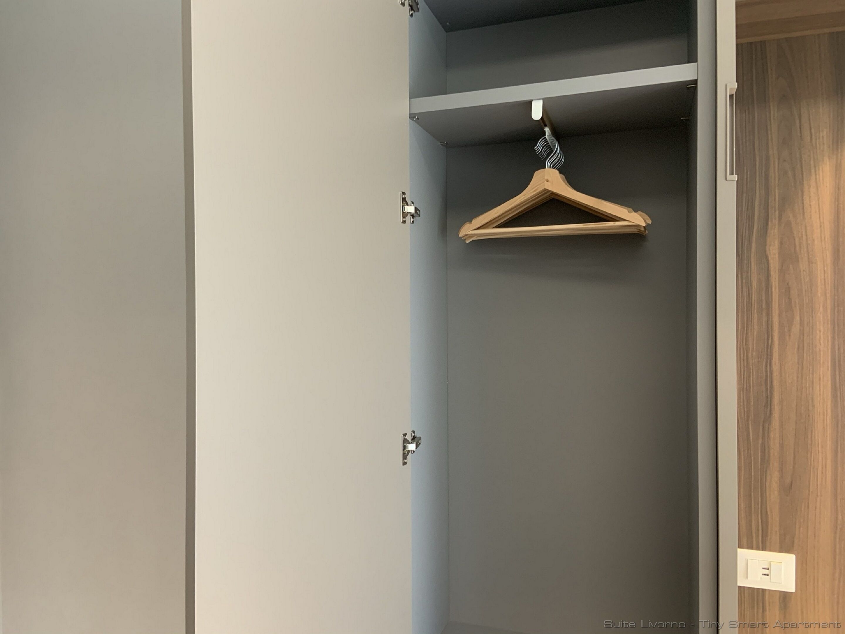 Ein Schrank mit einem hölzernen Kleiderbügel an einer Metallstange, einem Lichtschalter und einer Tür mit Holzvertäfelung.