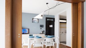A modern kitchen with white cabinets, a black door, and a dining area with white chairs and a table. - Suites Marilia Apartments (Livorno)