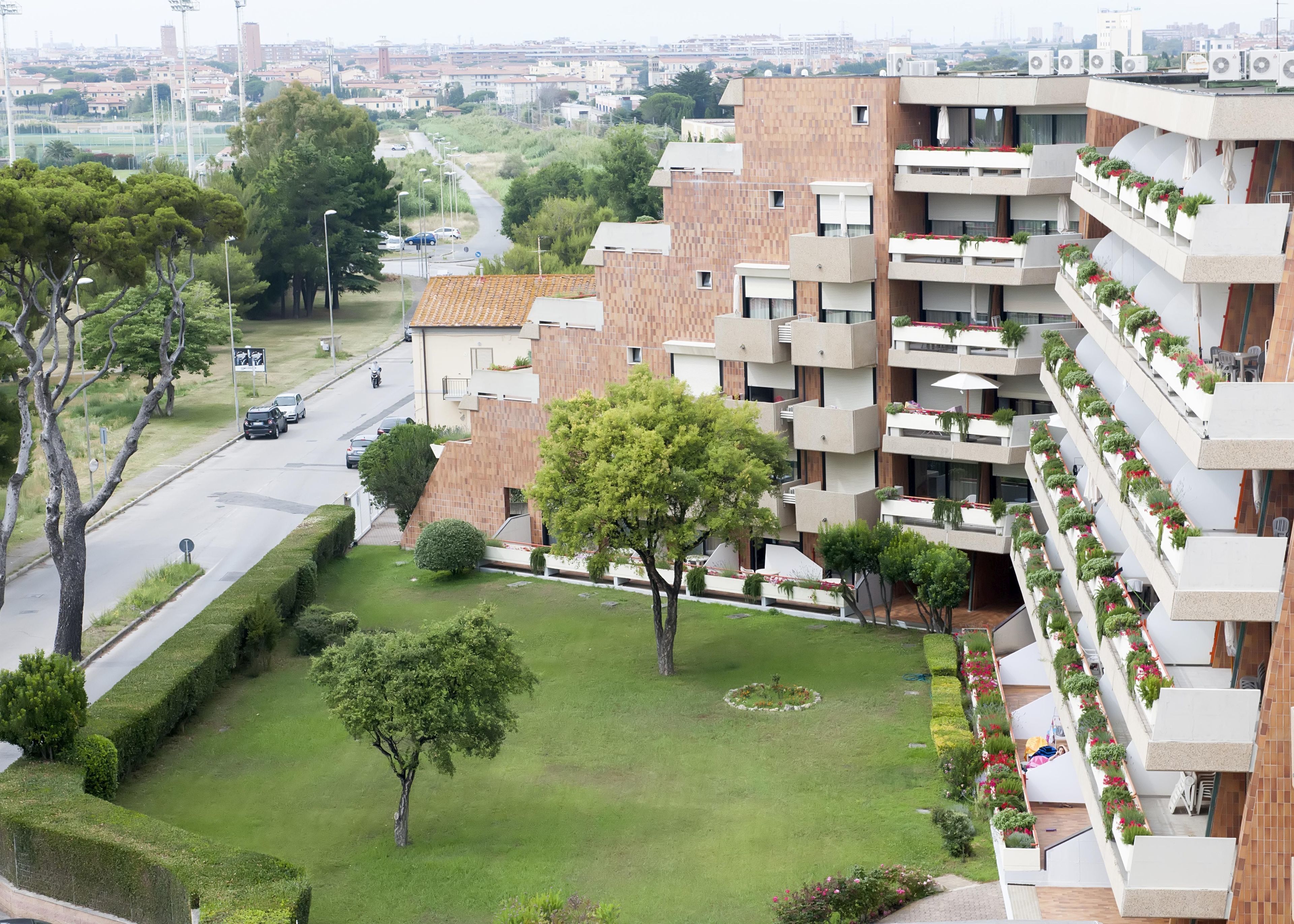 A modern apartment building with multiple balconies, a well-maintained lawn, and a road with cars passing by.