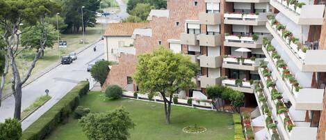 A modern apartment building with multiple balconies, a well-maintained lawn, and a road with cars passing by.