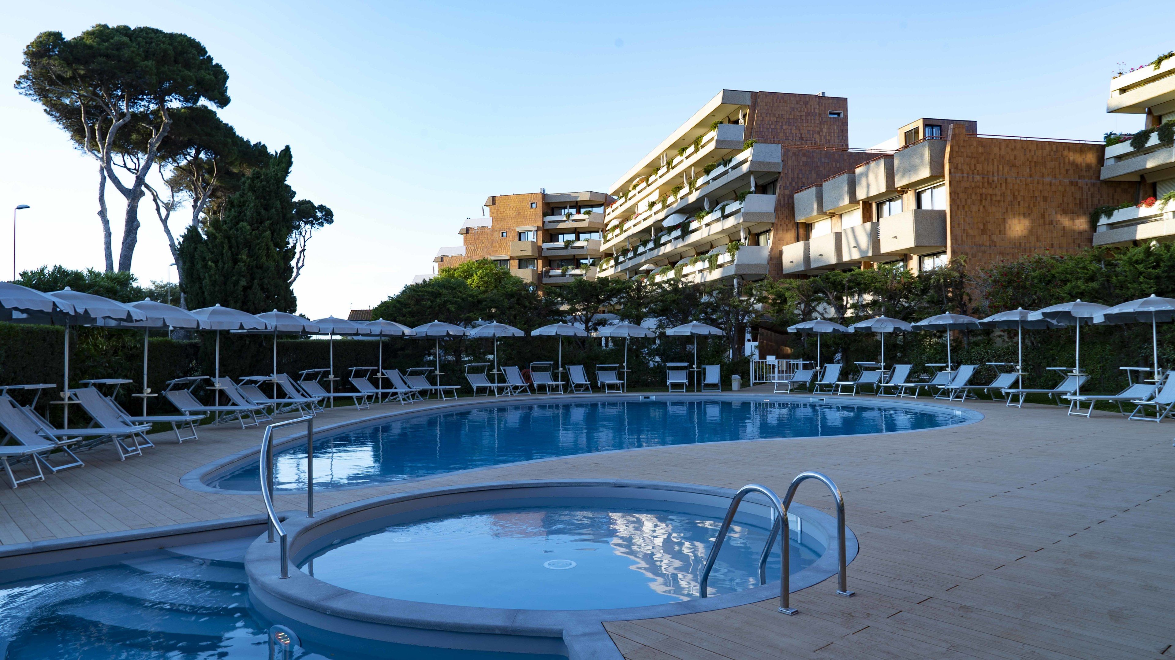 A swimming pool with lounge chairs and umbrellas, surrounded by buildings with balconies.