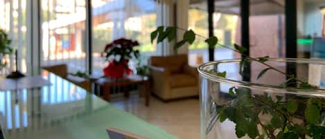 Ein modernes Hotelzimmer mit einem Glastisch, einer klaren Vase mit grünen Blättern und Blick durch große Fenster nach draußen.