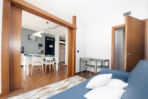 Una sala de estar moderna con un sofá azul, suelo de madera y una zona de comedor con sillas blancas y una mesa.