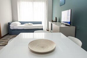 Ein Hotelzimmer mit einem weißen Tisch, einem blauen Sofa, einem Fernseher und einem Wasserkocher.
