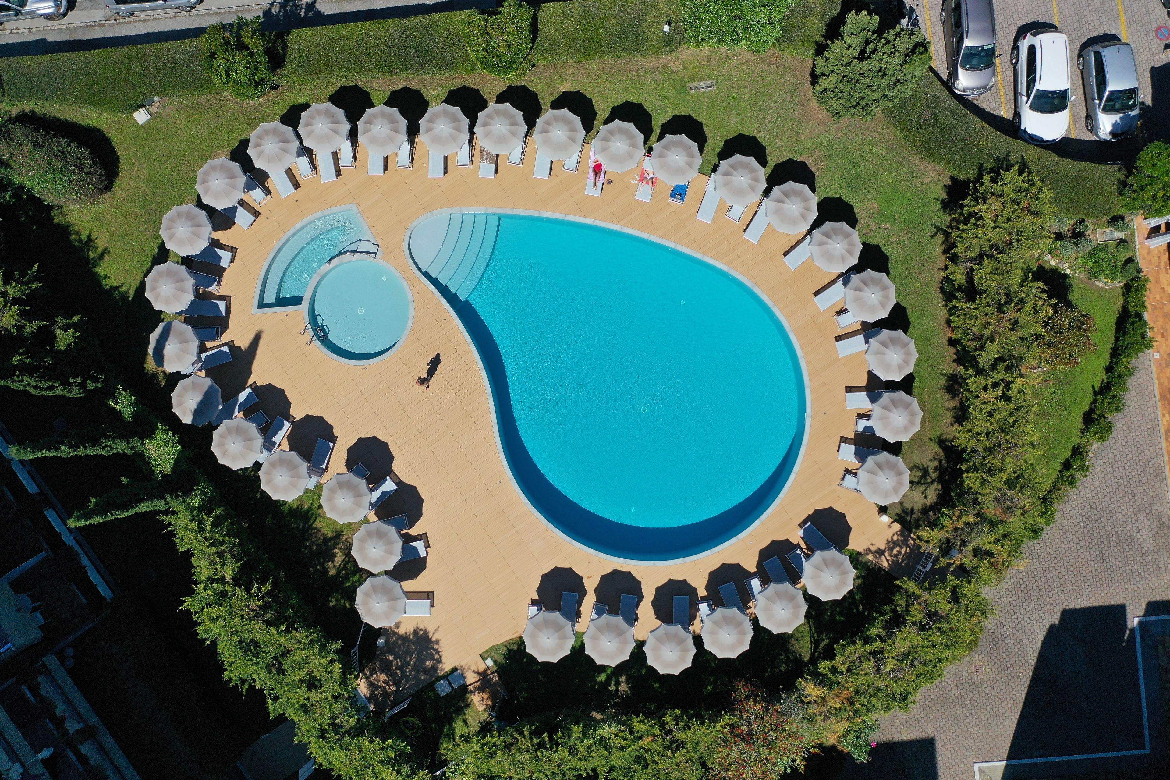 Une vue aérienne d’une piscine circulaire entourée de chaises longues et de parasols, avec une piscine plus petite à l’intérieur.