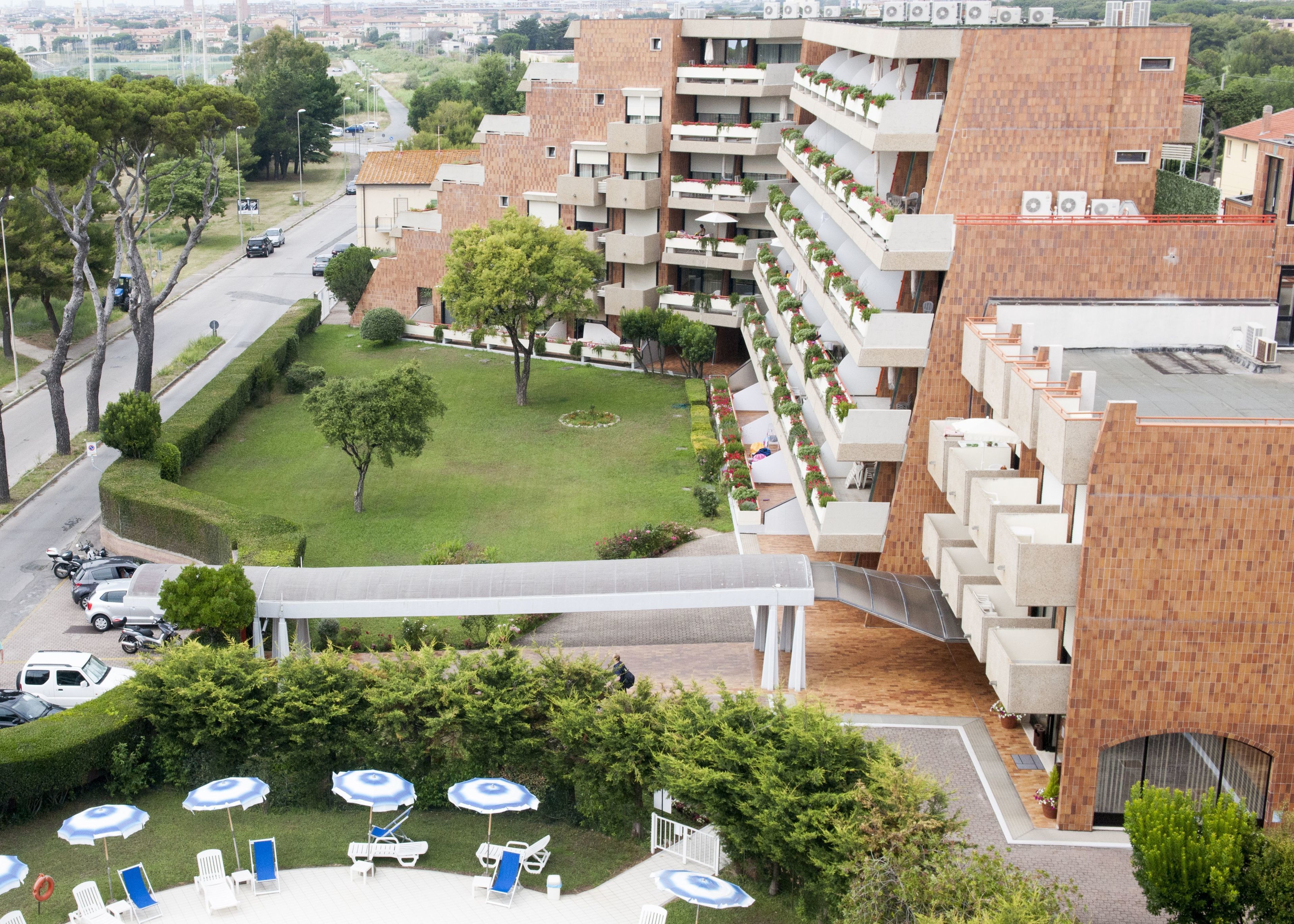 A multi-story residential building with balconies, a central courtyard, and a parking area with cars and a motorcycle.