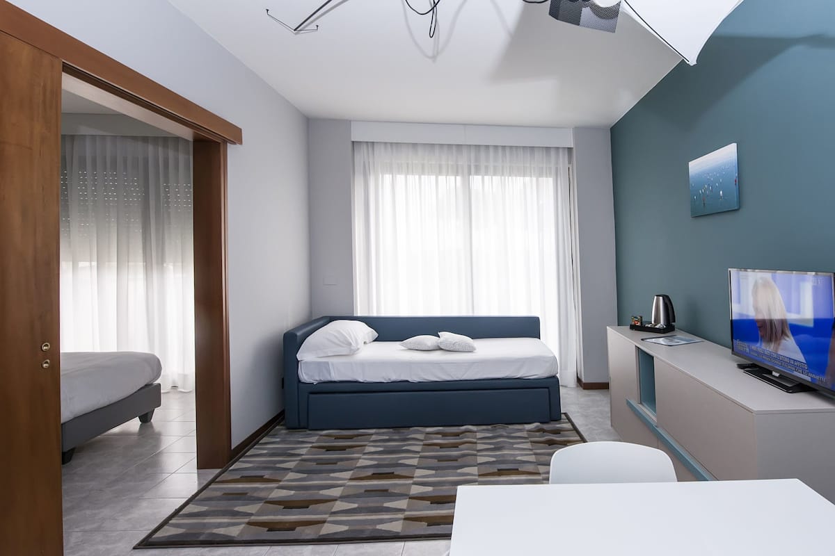 A modern hotel room with a bed, a desk, a television, and a window with curtains.