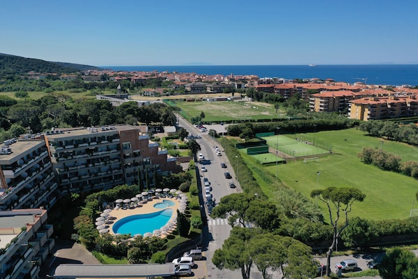 Un hotel de gran altura con piscina, una carretera con coches aparcados y vista al mar y a la ciudad al fondo.