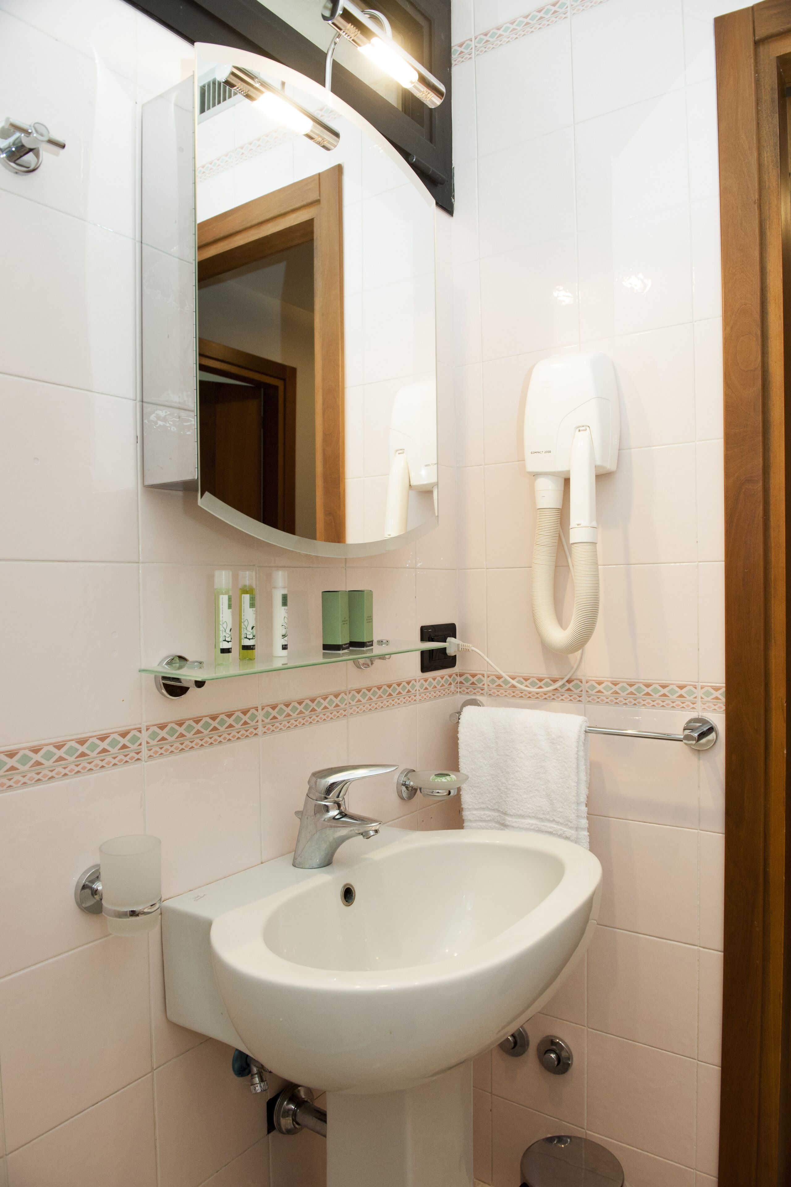 Un baño con lavamanos blanco, un espejo, toallero y secador de pelo fijado a la pared.