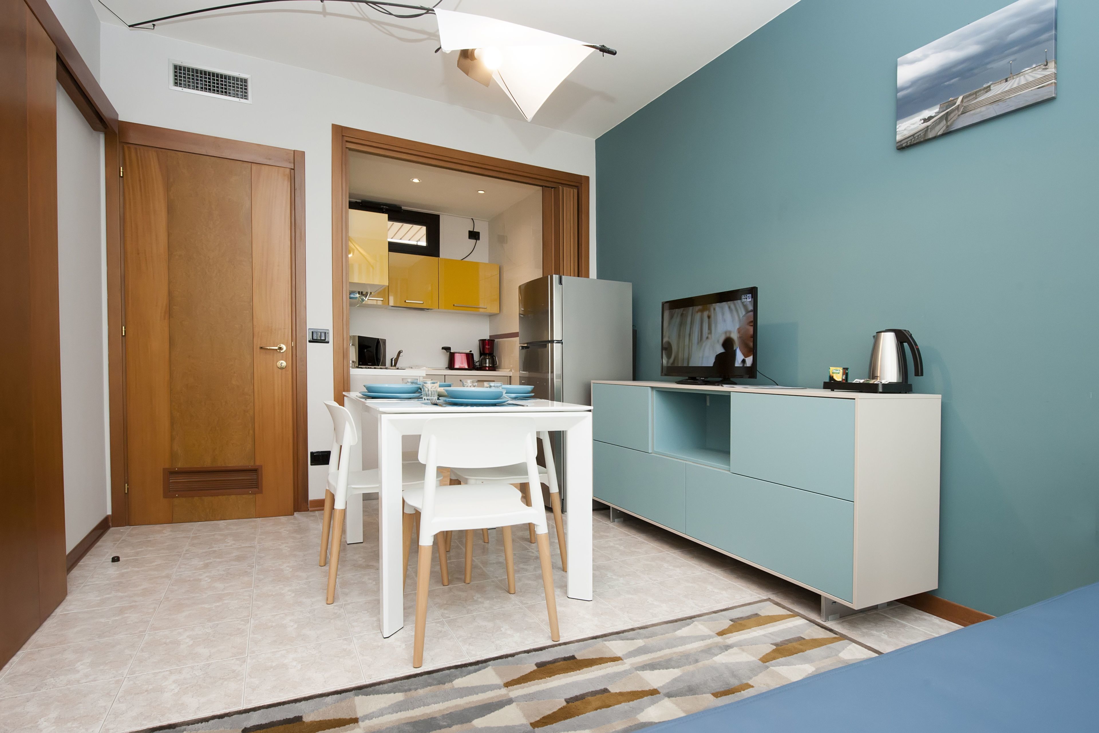Una cocina compacta con zona de comedor, un refrigerador blanco y un mueble de color aguamarina.