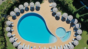 An aerial view of a pool area with multiple sun loungers and umbrellas arranged in a circular pattern around a central swimming pool. - Suites Marilia Apartments (Livorno)