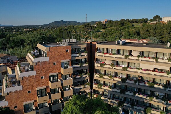 Un hôtel à plusieurs étages doté de balcons, d’un espace extérieur aménagé et offrant une vue sur le paysage environnant.