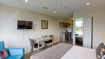 A hotel room with a bed, a desk with a chair, a television, and a kitchenette.