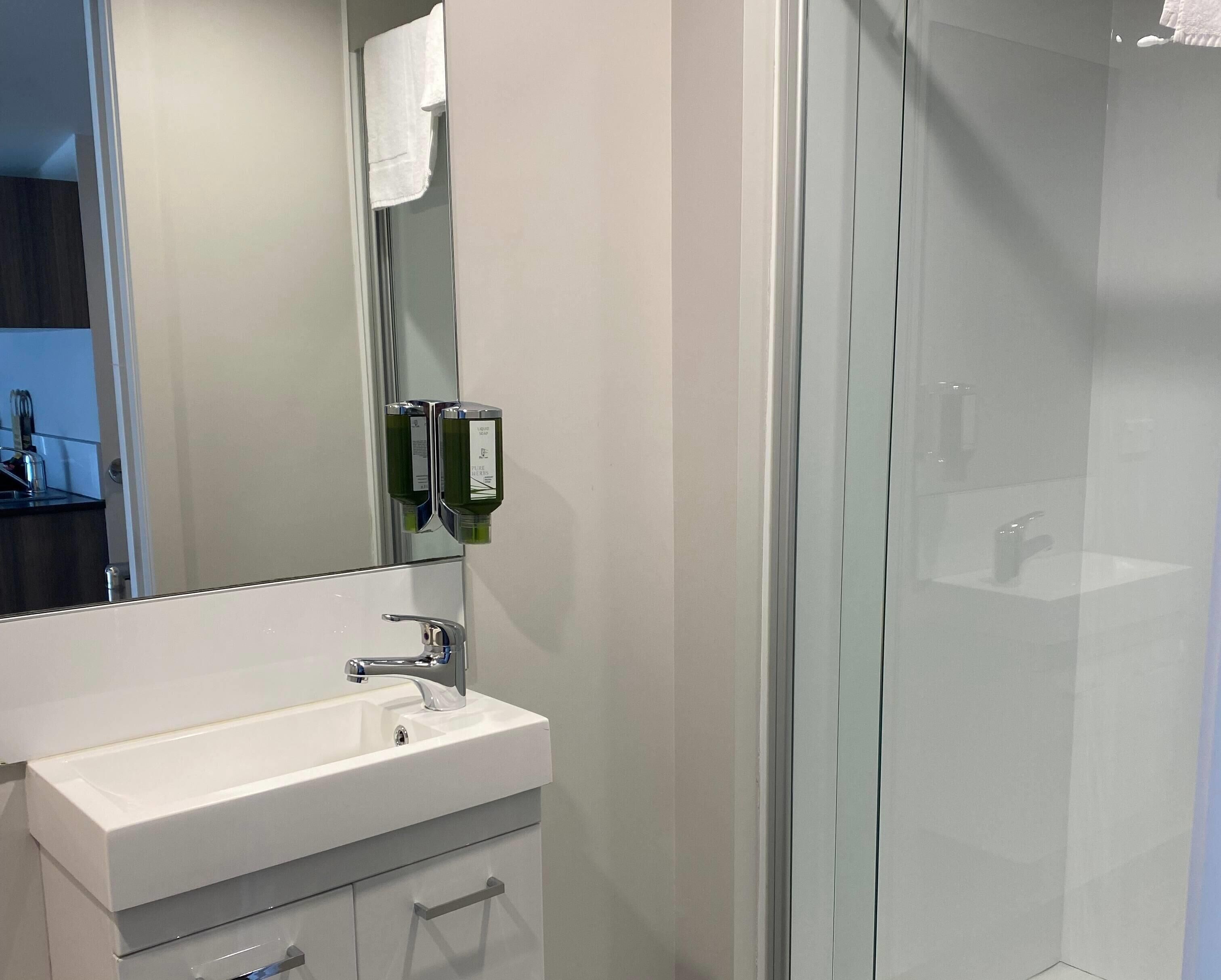 A modern bathroom with a glass shower enclosure, a white sink with a chrome faucet, and a mirror with a towel hanging on it.
