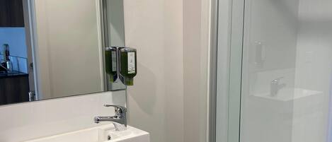 A modern bathroom with a glass shower enclosure, a white sink with a chrome faucet, and a mirror with a towel hanging on it.