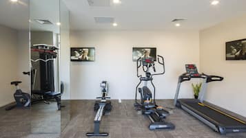 A home gym with a treadmill, stationary bike, elliptical, and weight bench.