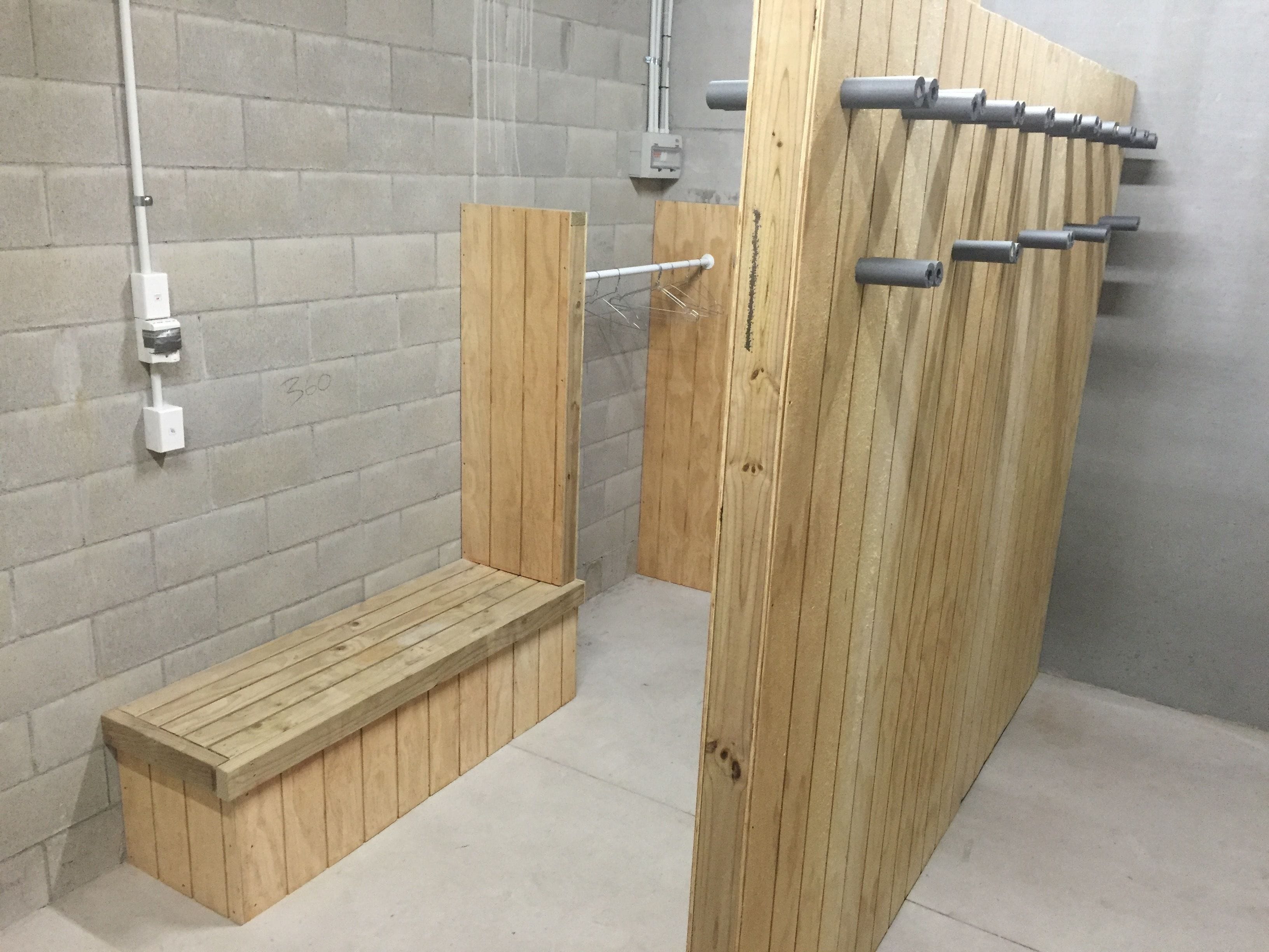Cabina de bany de fusta amb una cadira, un penjador de tovalloles i una presa elèctrica fixada a la paret.