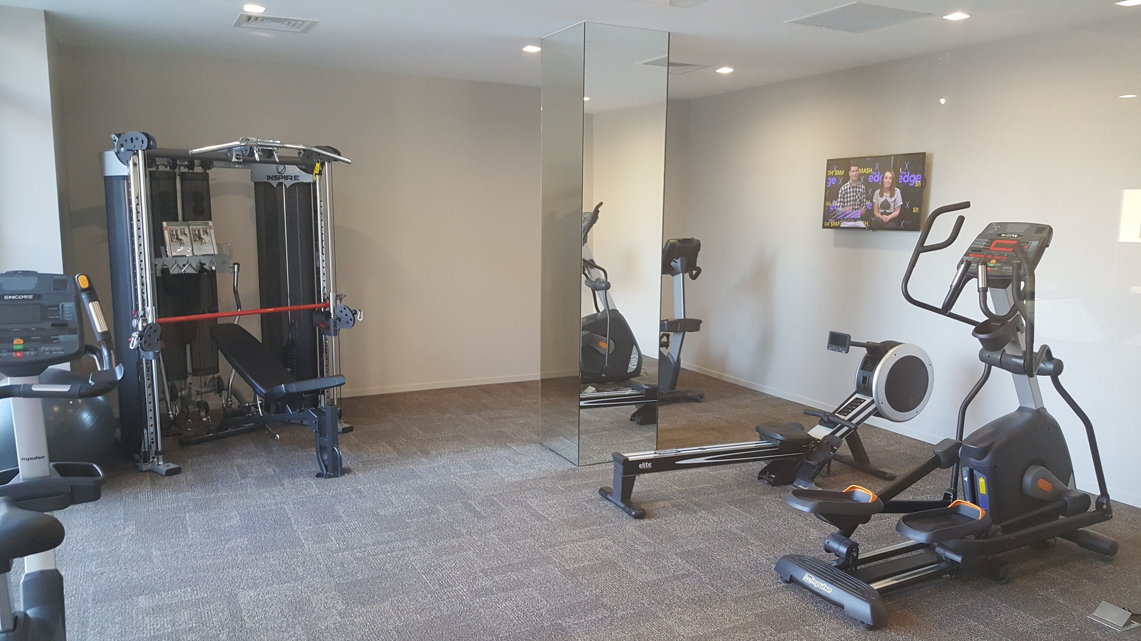 Ein Fitnessstudio mit Cardiogeräten, Krafttrainingsgeräten und einer Spiegelwand.