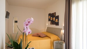 A hotel room with a bed, a bedside table with a remote control, a potted plant, and a wall-mounted artwork. - Xenia Hotel (Villasimius)