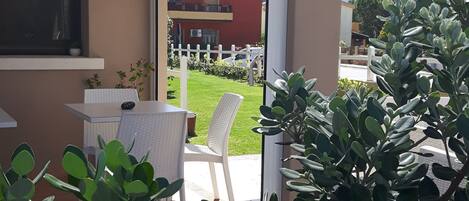 A covered patio area with a table and chairs, surrounded by greenery.